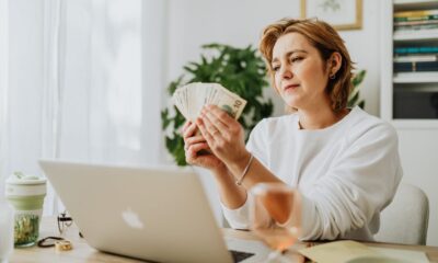 Person calculating daily side hustle earnings on a laptop with cash nearby