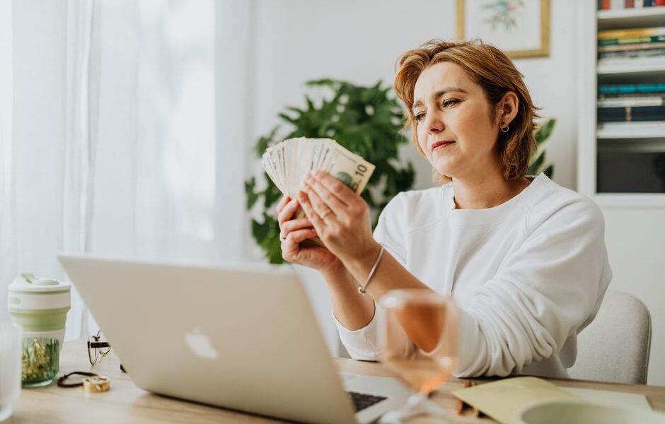 Person calculating daily side hustle earnings on a laptop with cash nearby