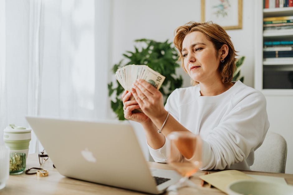 Person calculating daily side hustle earnings on a laptop with cash nearby