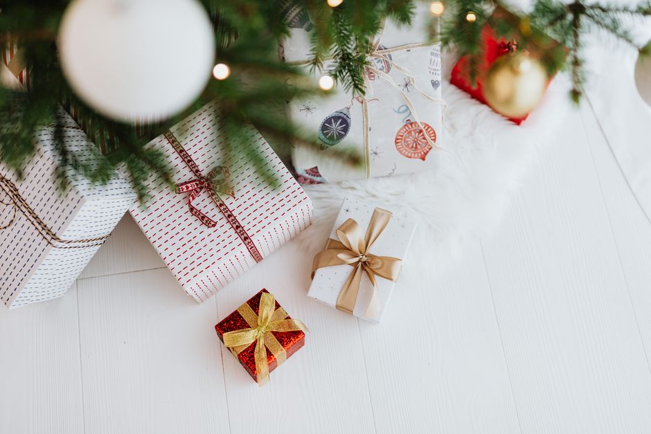 Stack of wrapped Christmas gifts in various sizes under a decorated tree